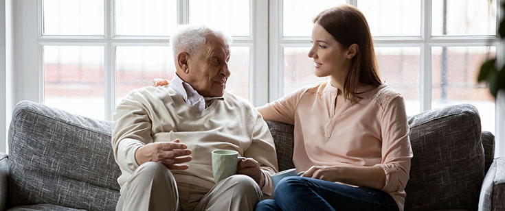Elderly man talks with daughter on couch Elderly man talks with daughter on couch